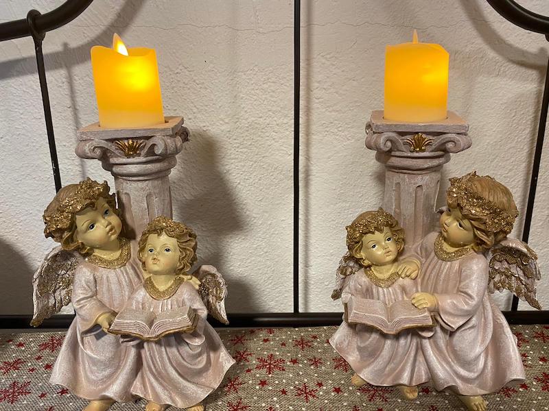 2 figuras de ángeles delante de una columna que sostiene una vela